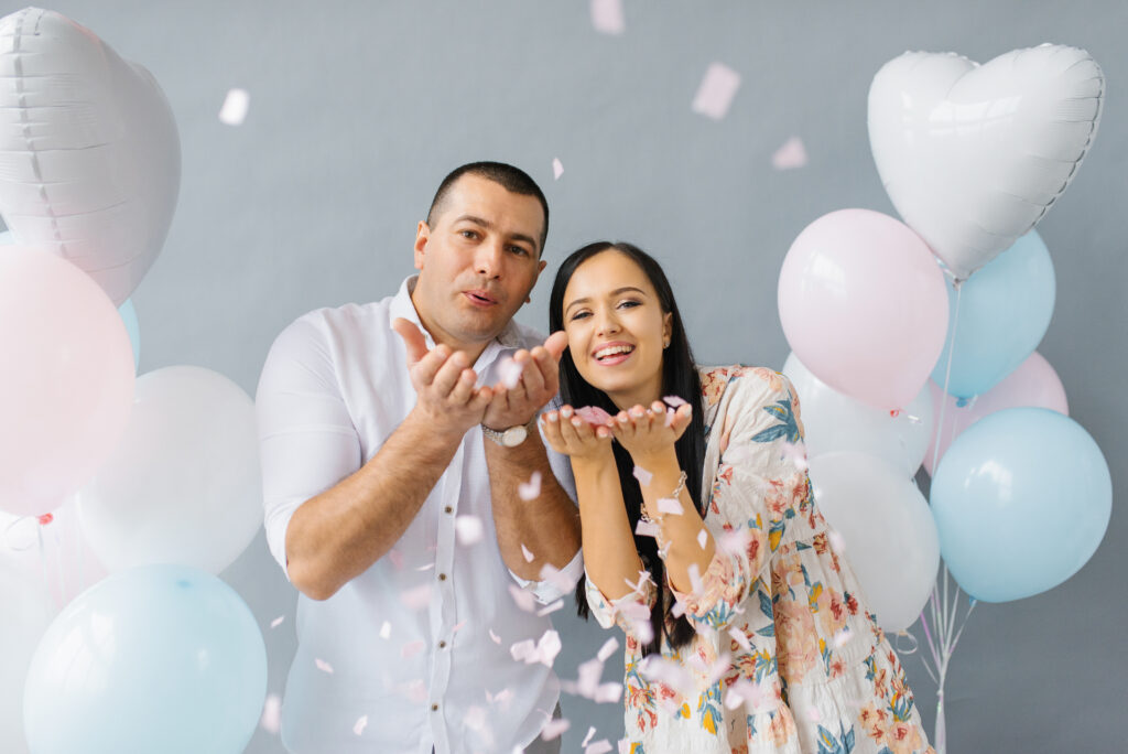 happy couple in love blowing on confetti in honor of their love on the background of balloons and smiling, laughing happy couple in love blowing on confetti in honor of their love on the background of balloons and smiling, laughing
